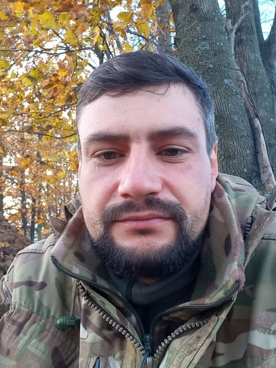 Портрет Андрія Степановича Турика з темним волоссям та бородою, одягненого у військову форму, з деревами та жовтим листям на задньому плані.
